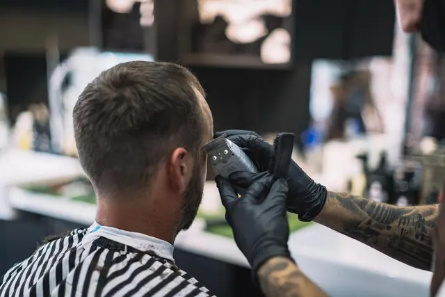 A gloved barber finishing a neckline with clippers